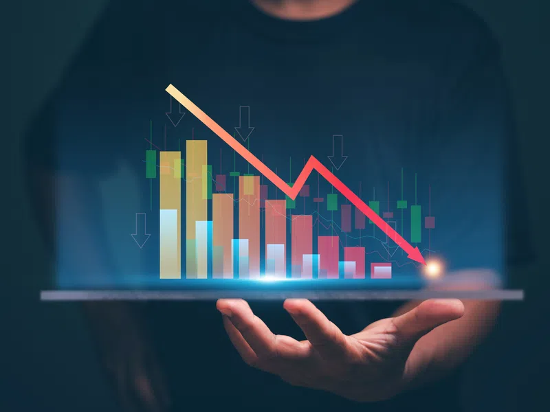 Hand holding a digital tablet projecting a downward trending financial bar and line graph with arrows.