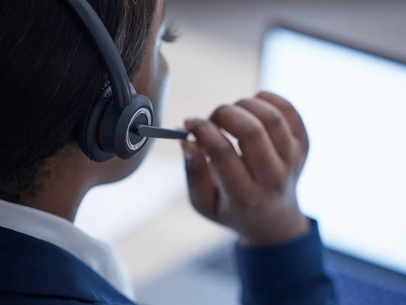 Close-up of a person wearing a headset and working on a laptop, likely a customer service or call center agent.