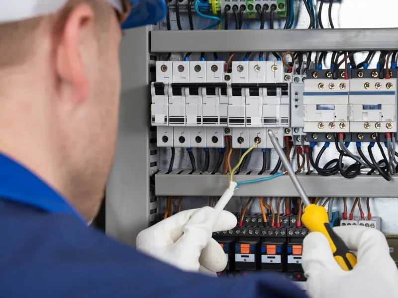 Electrician wearing gloves working on circuit breakers inside an electrical panel with tools and wires.
