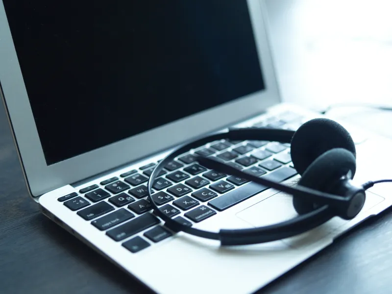 Black headset resting on the keyboard of a silver laptop with a blank screen on a wooden surface