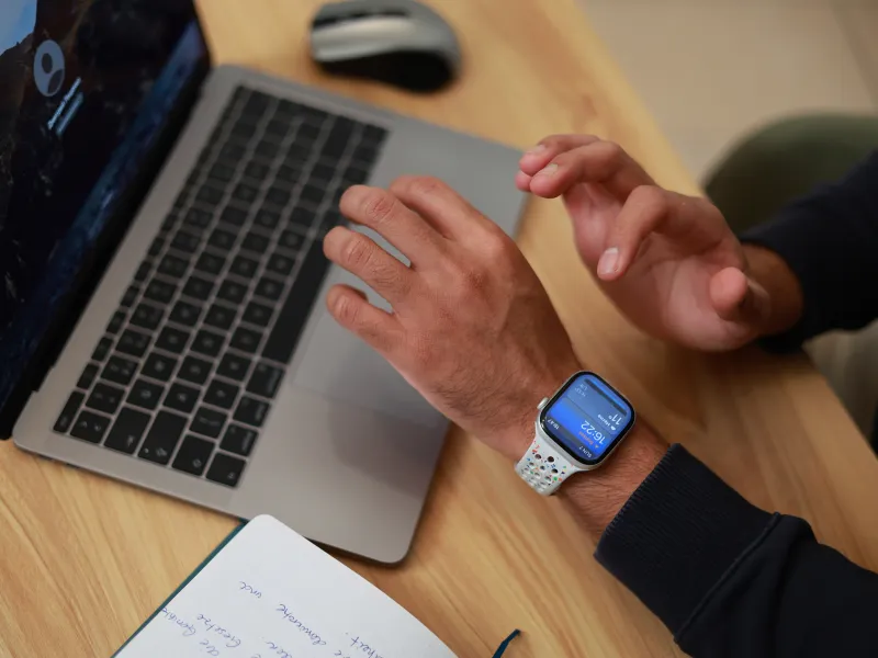 Person using a laptop with an Apple Watch displaying time and fitness data on the wrist.