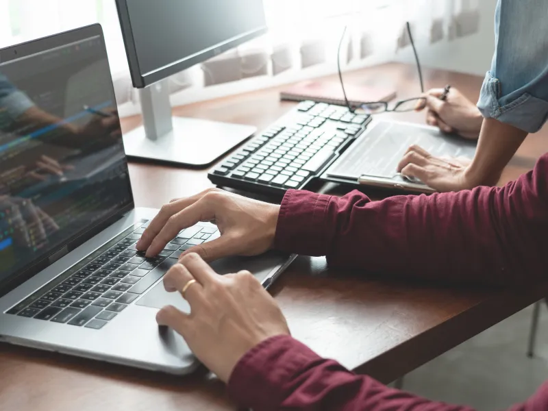 Two developers working on coding with multiple screens and laptop in a modern office setting.