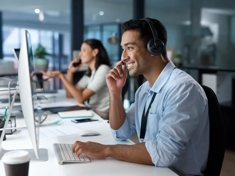 Smiling customer service representative wearing headset working at desk with computer in modern office