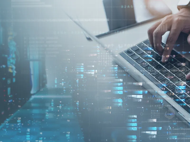 Hands typing on laptop keyboard with digital data overlay and server racks in a technology setting.
