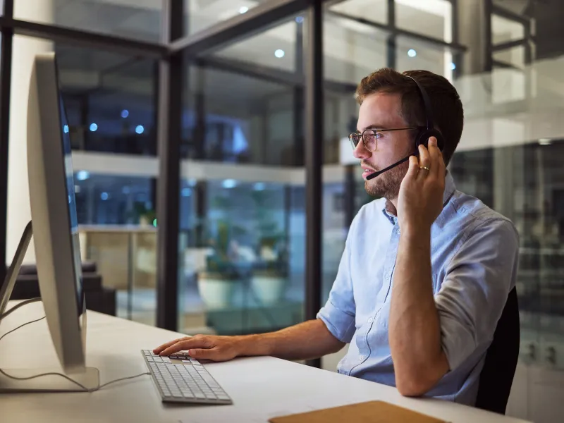 Customer support agent wearing headset working on computer in modern office at night