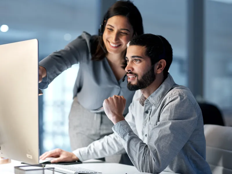 Two coworkers collaborate on a computer project in a modern office with focused expressions and teamwork.