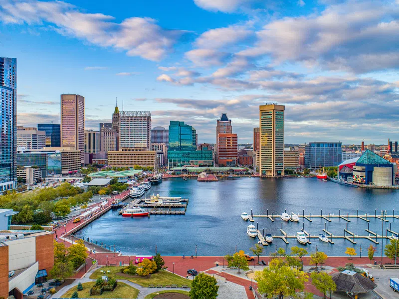 Baltimore Inner Harbor skyline with boats, docks, and colorful city buildings under a cloudy blue sky.