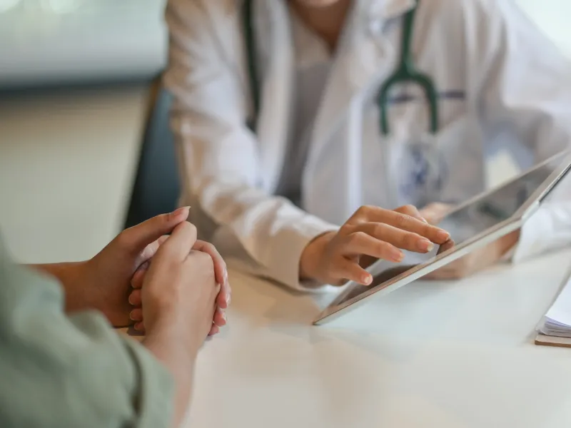 Doctor consulting patient using digital tablet with clipboard on table in medical office