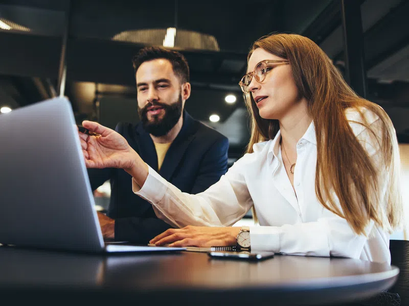 Two professionals collaborating over a laptop in a modern office setting with focused expressions.