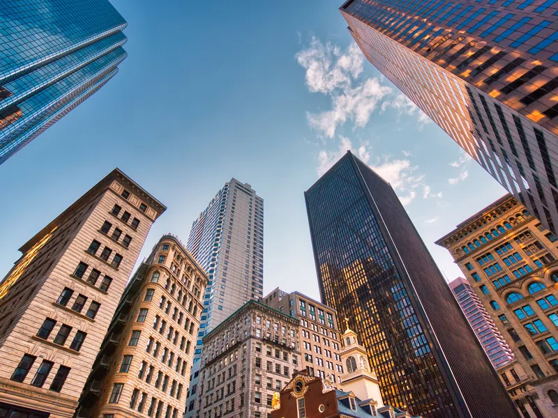 View looking up at diverse skyscrapers and historic buildings under a bright blue sky in a city center.