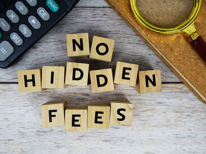 Wooden blocks spelling No Hidden Fees next to a calculator and magnifying glass on a wooden table.