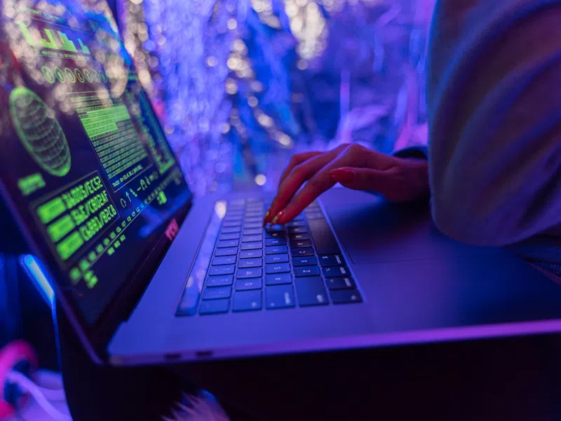 Person typing on laptop with green digital data overlays in a blue and purple ambient light environment.