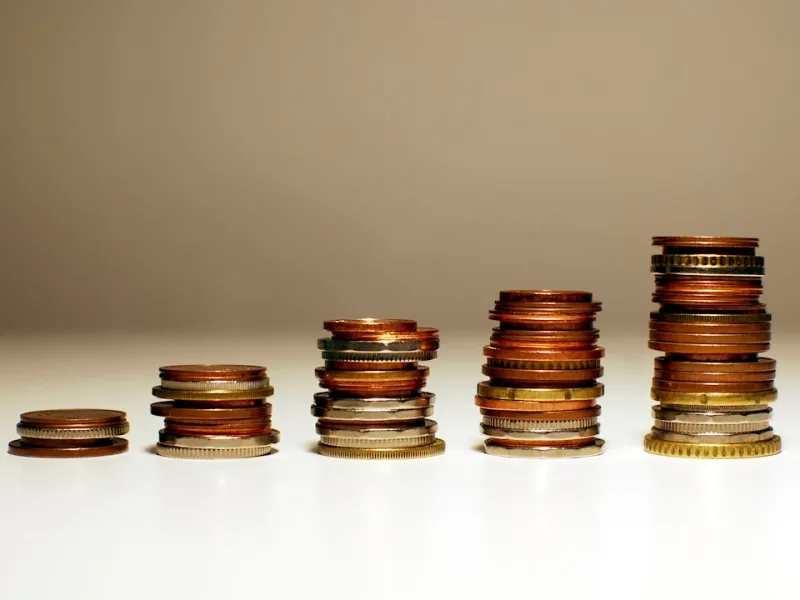 Stacks of mixed coins arranged in ascending order on a white surface against a neutral background.