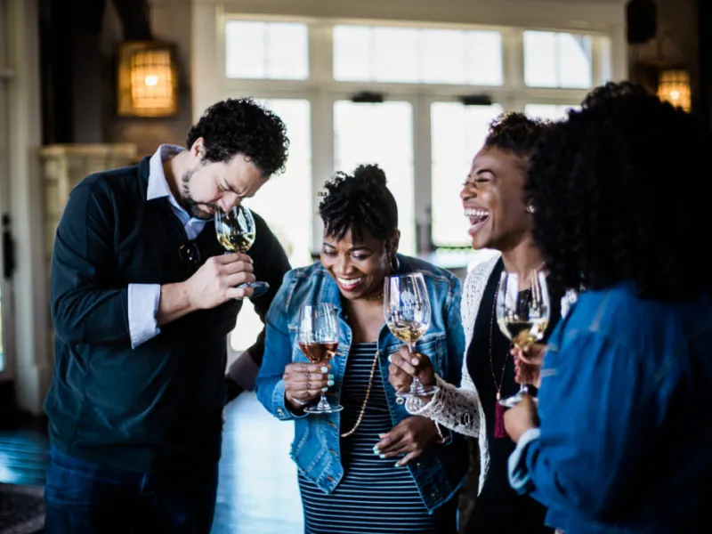 Group of friends enjoying wine tasting and laughing together in a cozy, well-lit room.