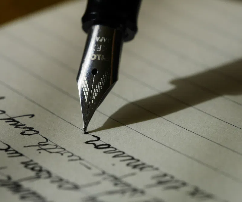 Close-up of a fountain pen writing cursive text on lined paper with shadow cast to the side