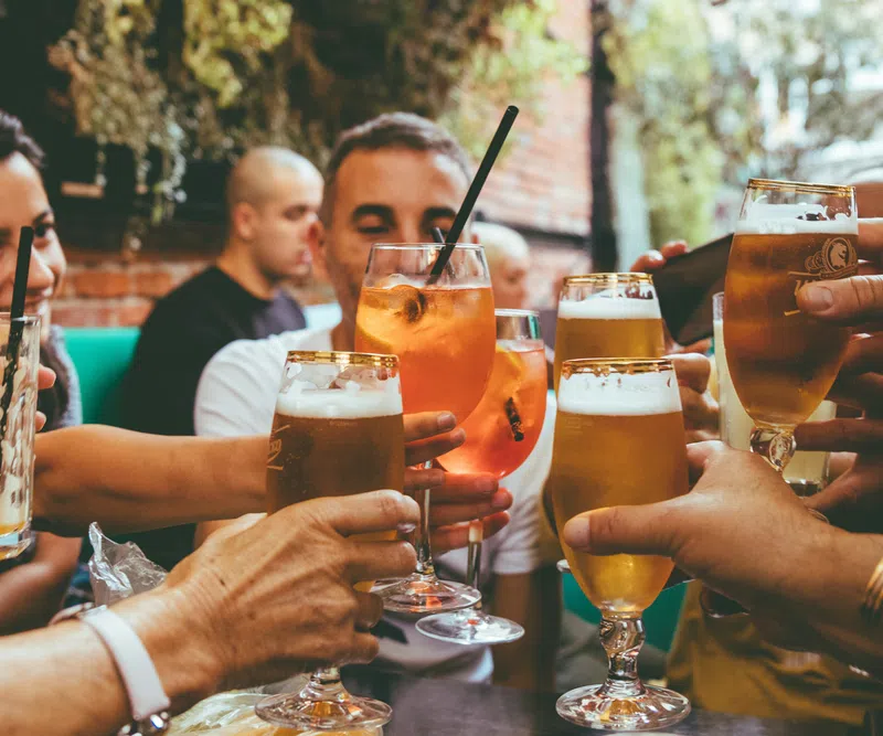 Group of friends clinking glasses with beer and cocktails at an outdoor social gathering.