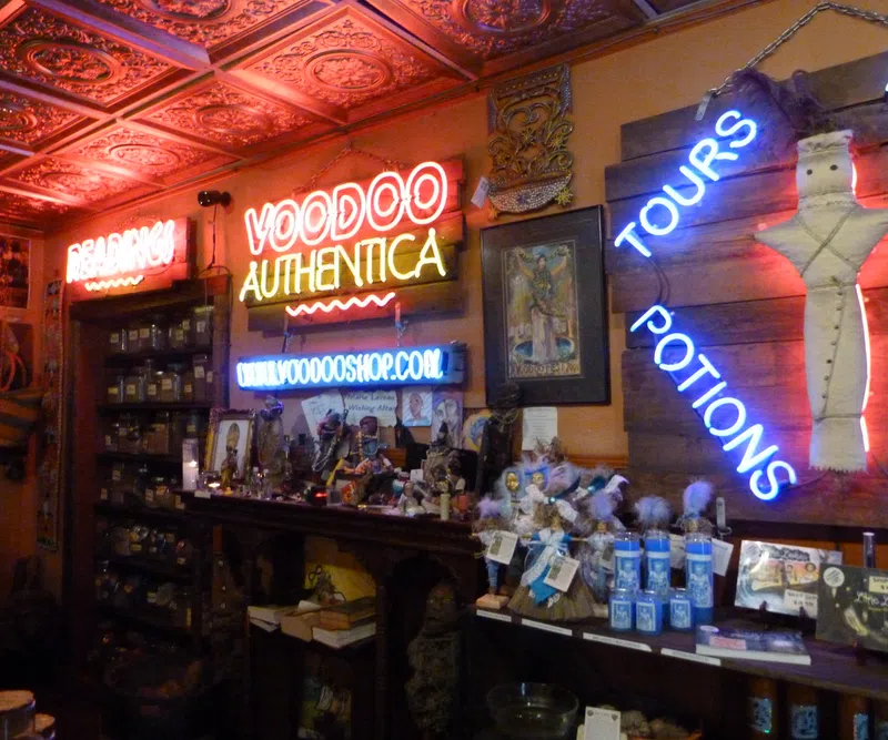 Interior of a voodoo shop with neon signs, shelves of jars, potions, dolls, and mystical items under ornate ceiling tiles.