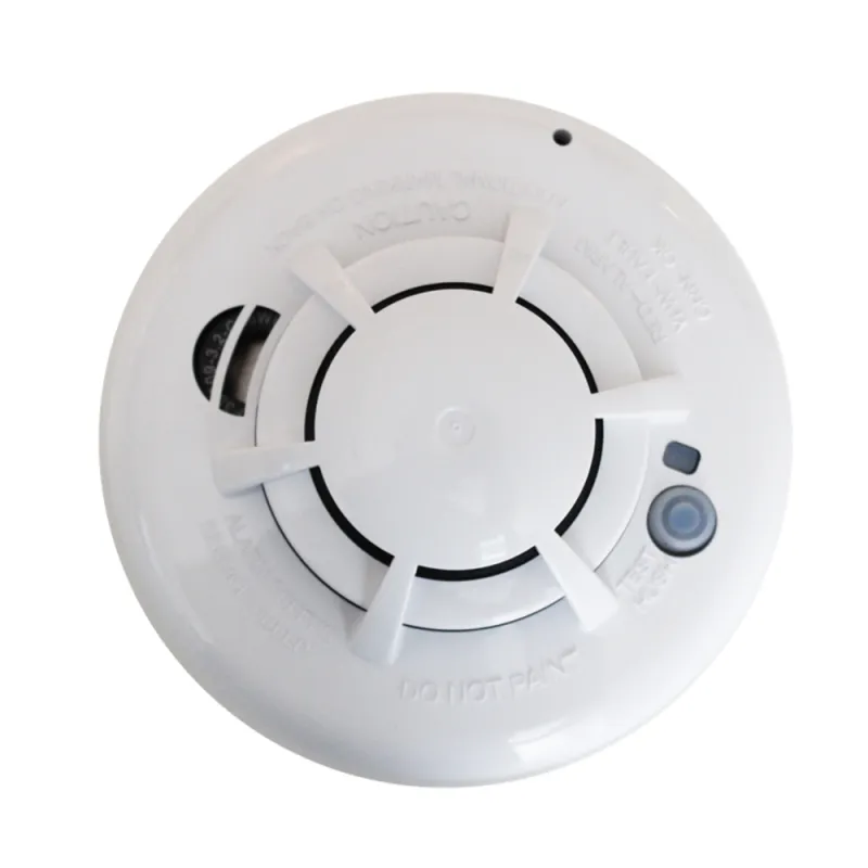 Round white smoke detector with sensor, test button, and warning text on a white background.