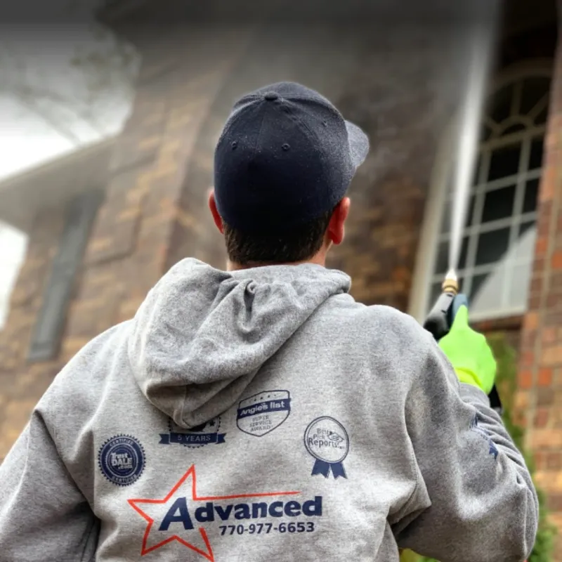 A man in a gray hoodie sprays a building exterior, showcasing professional cleaning services.