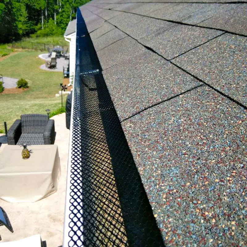 Close-up of shingled roof edge with gutter guard installed, showcasing landscaping below.