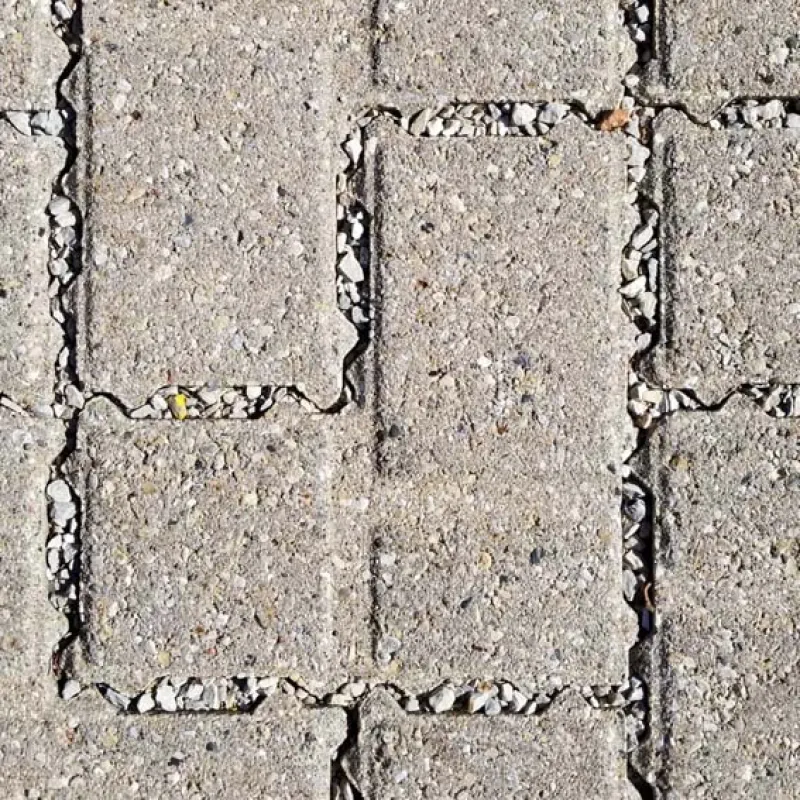 Close-up of gray concrete paving stones with small gravel filling the gaps between the blocks on ground.