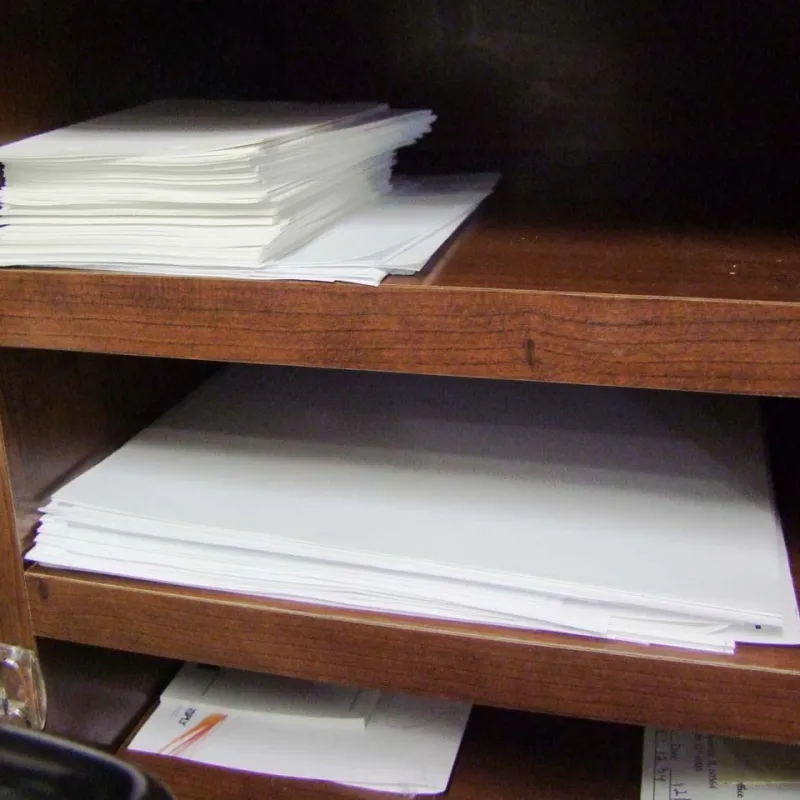 Stack of white papers neatly organized on wooden office shelves with pens and calendar nearby