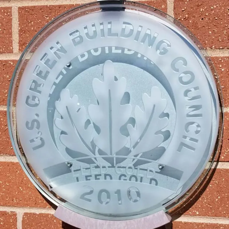 Frosted glass U.S. Green Building Council LEED Gold 2010 plaque mounted on brick wall.