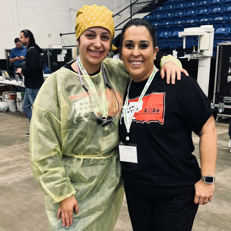 Two smiling women posing together in a large indoor venue, one wearing medical scrubs and the other in casual attire.