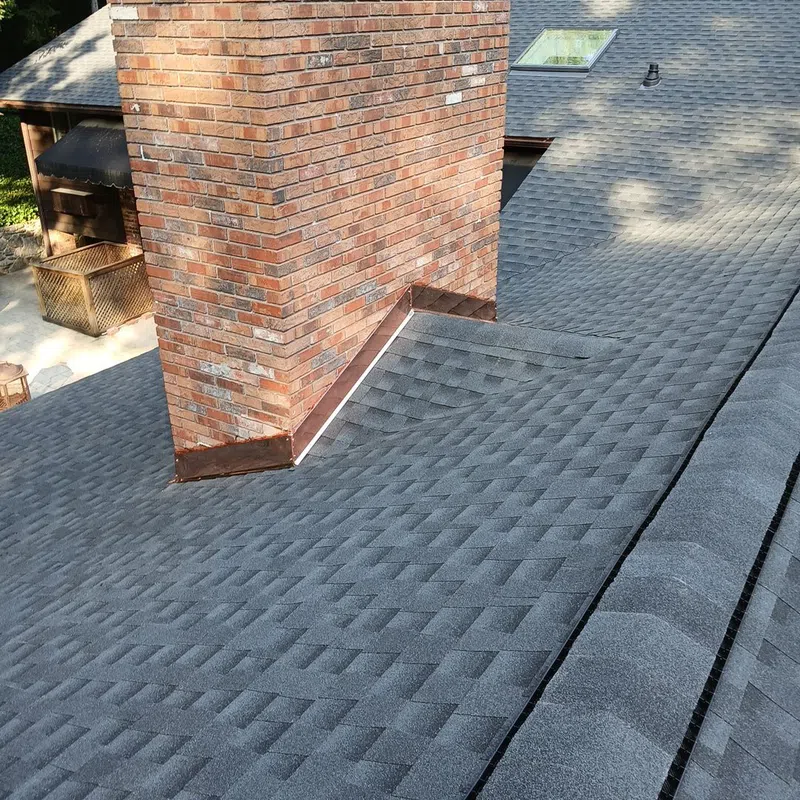 Close-up of a brick chimney with copper flashing on a gray shingled roof under natural light.