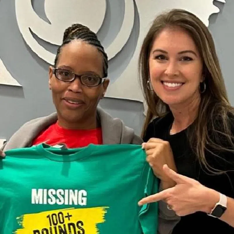 Two women smiling holding a green t-shirt with the text Missing 100+ Pounds No Reward Do Not Report If Found