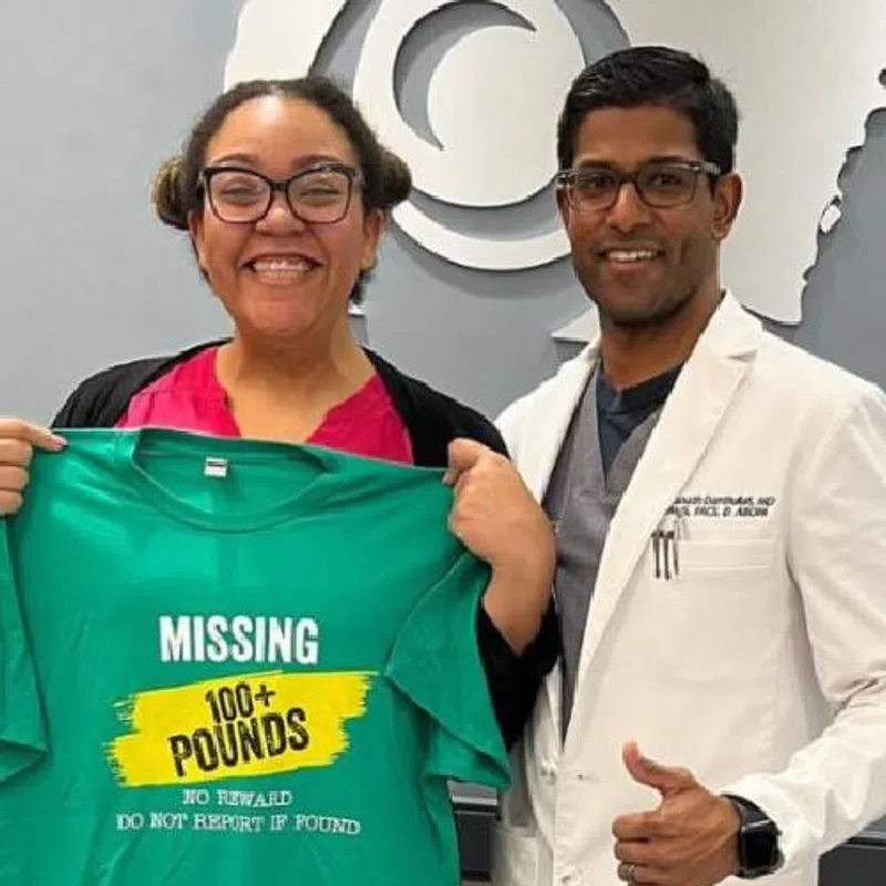 Smiling woman holds a green shirt with weight loss message standing next to doctor giving thumbs up.