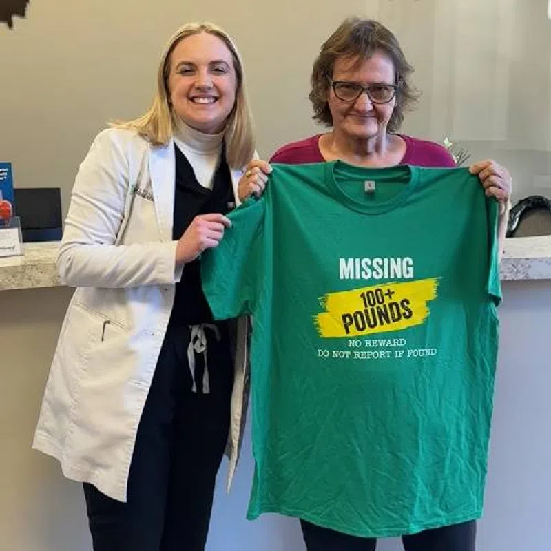Two smiling women holding a green shirt that reads Missing 100+ Pounds No Reward Do Not Report If Found