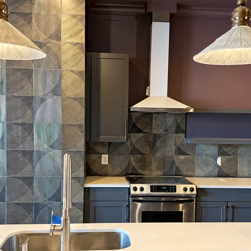 Modern kitchen with geometric tile backsplash, stainless steel stove, gray cabinets, and a white island with a sink.