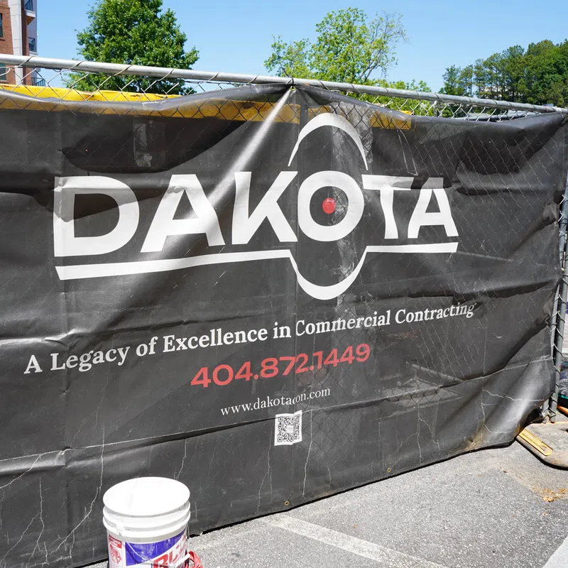 Black Dakota construction banner on chain link fence with commercial contracting contact info outdoors.