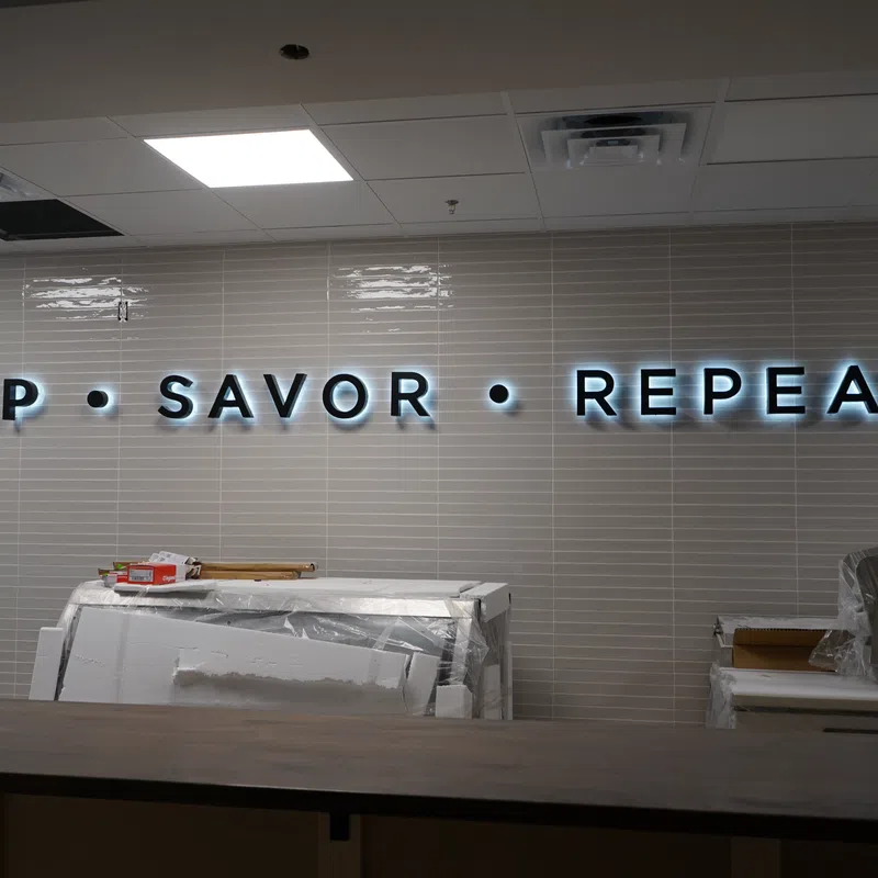 Illuminated wall sign reading Sip Savor Repeat in a modern interior with unpacked boxes and construction materials.