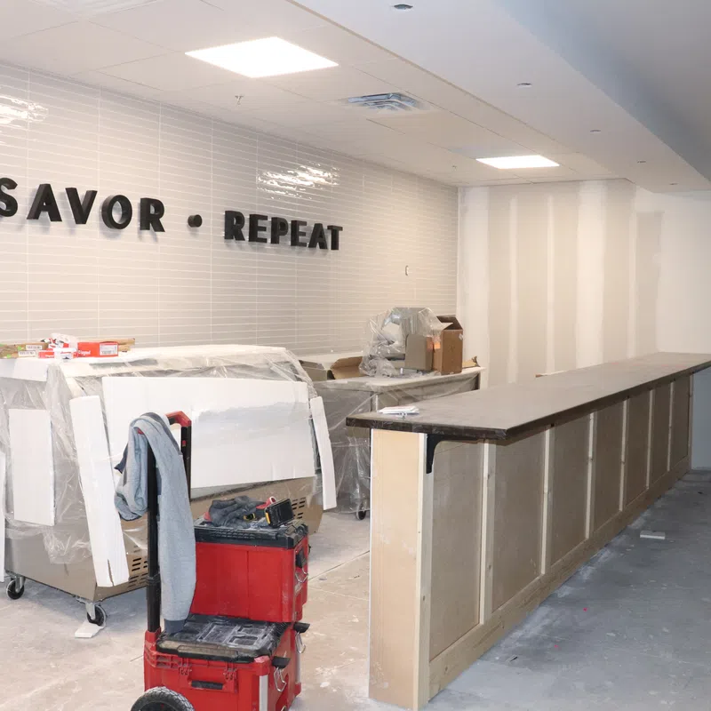 Under-construction restaurant interior with slogan Savor Repeat on tiled wall and bar counter being built.