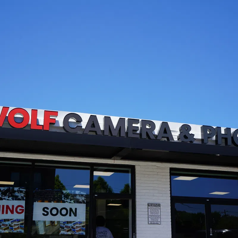 Storefront of Wolf Camera & Photo with a clear blue sky and Coming Soon signs in the windows.