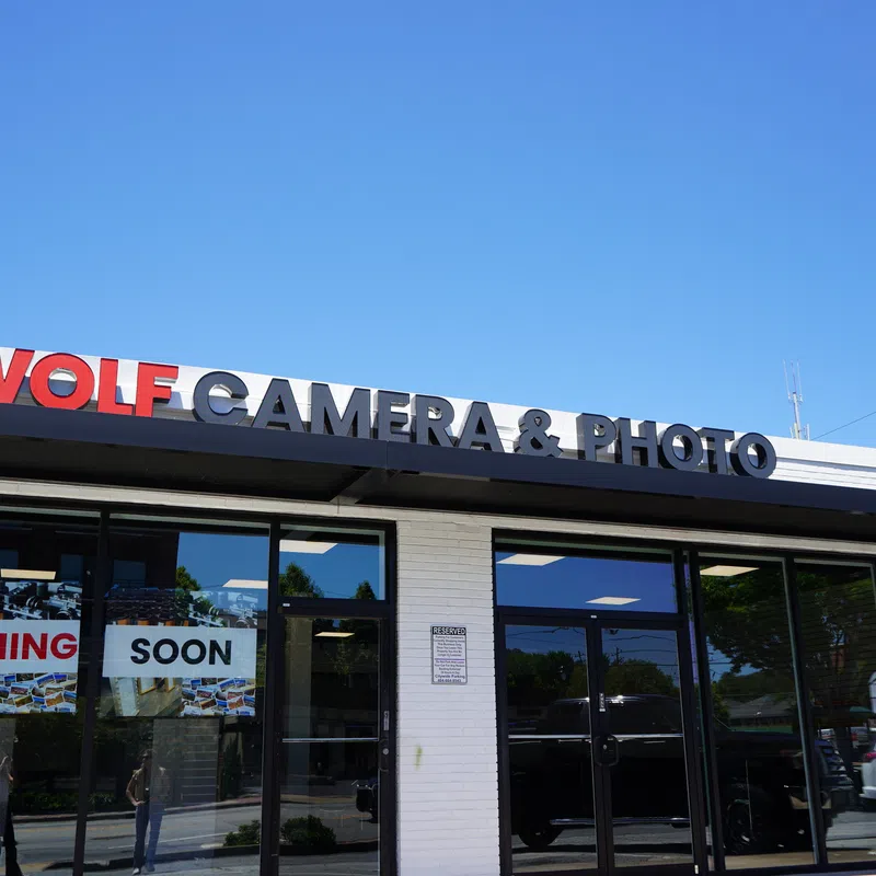Storefront of Wolf Camera & Photo with signage and Coming Soon banners under a clear blue sky.