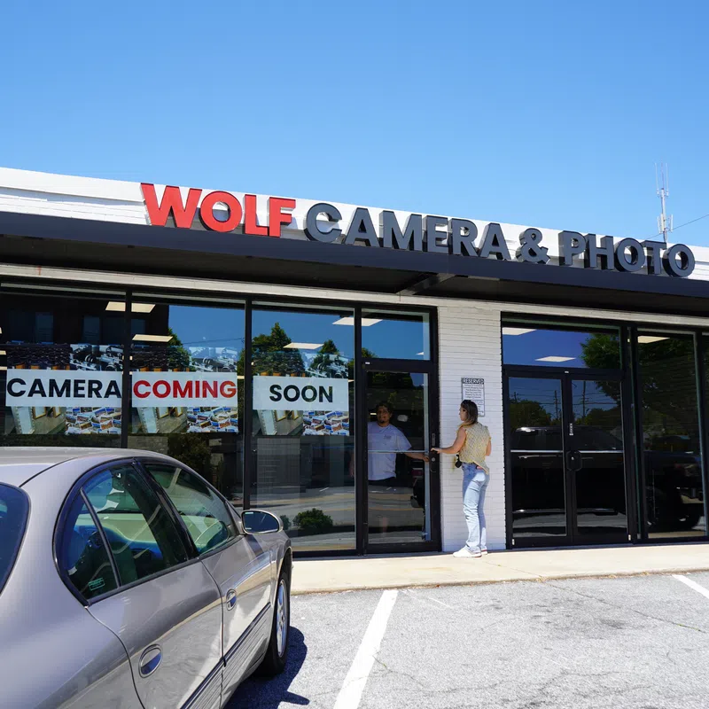 Wolf Camera & Photo store front with signs announcing the camera shop coming soon and people entering the store.