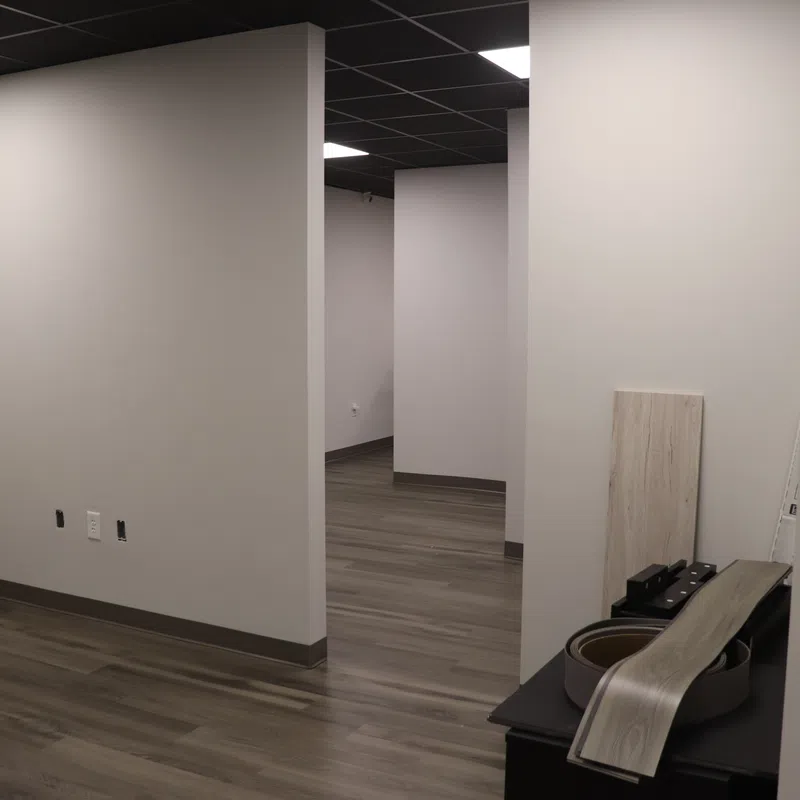 Empty office space with gray walls, wood-look flooring, and various building materials and tools inside.
