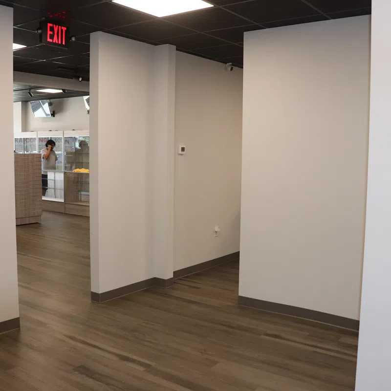 Empty modern office space with wood-look flooring, white walls, and a ceiling with black tiles and exit sign.