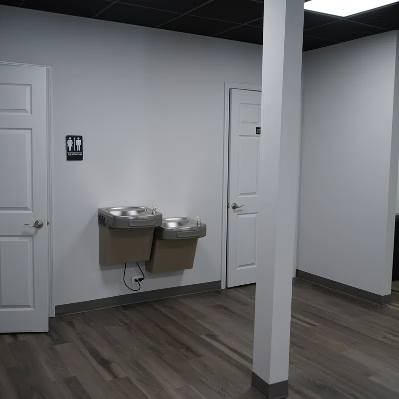 Interior of a modern indoor space with two white doors, dual water fountains, and wood-look flooring.