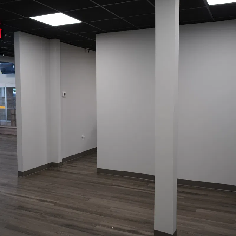 Empty office space with gray walls, wood flooring, and black tiled ceiling with exit sign.