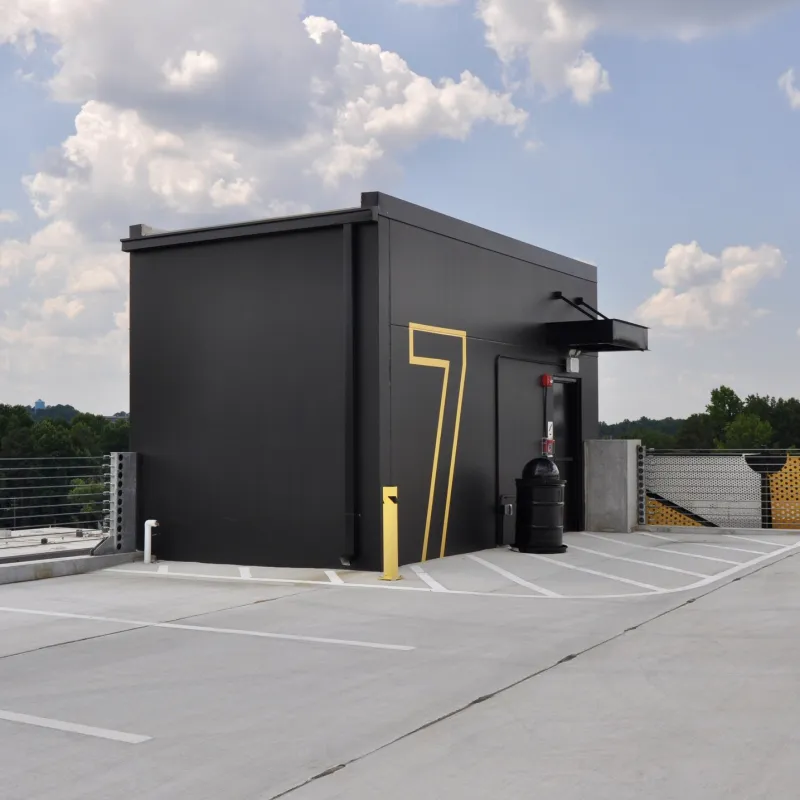 Empty rooftop parking lot with a black structure marked with a large yellow number 7 under cloudy blue sky.