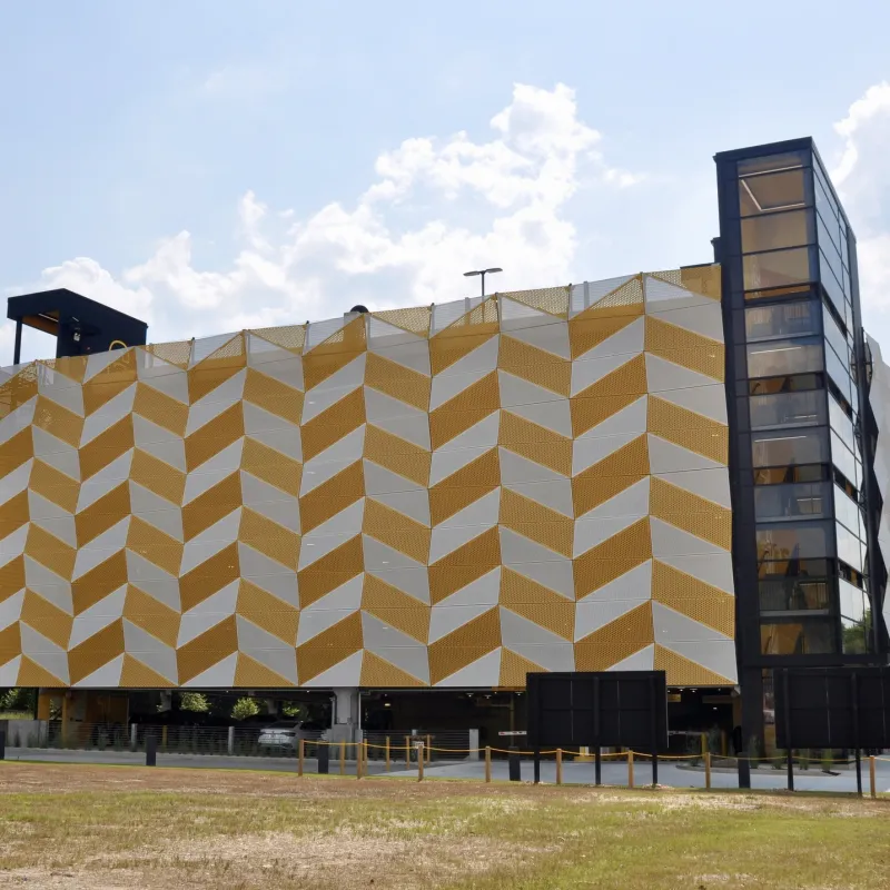 Modern building with yellow and white geometric patterned facade and glass elevator under a partly cloudy sky