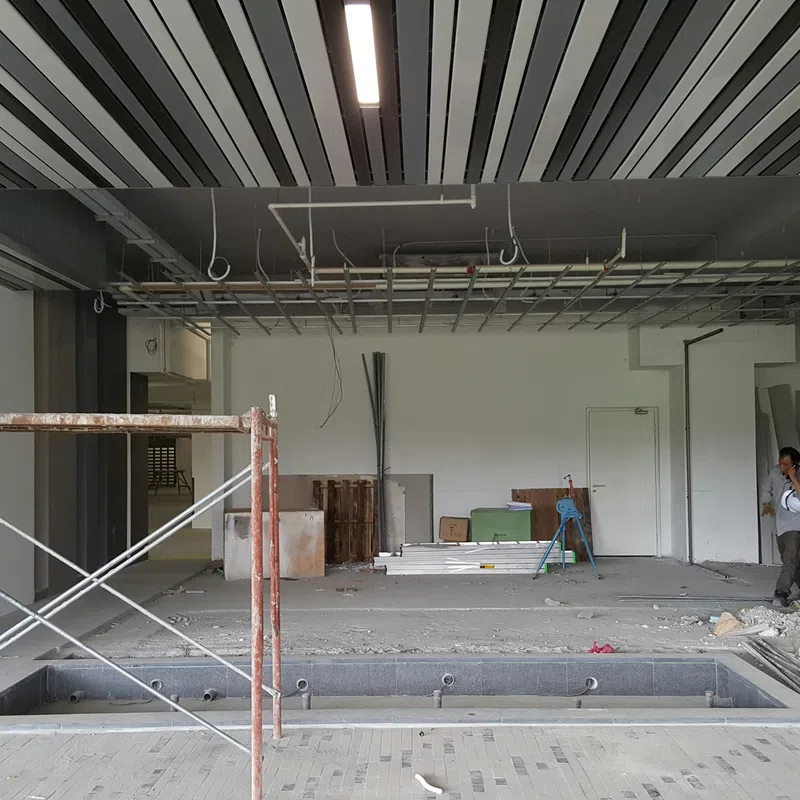 Indoor construction site with ceiling grid, scaffolding, workers, and open floor pit in progress.