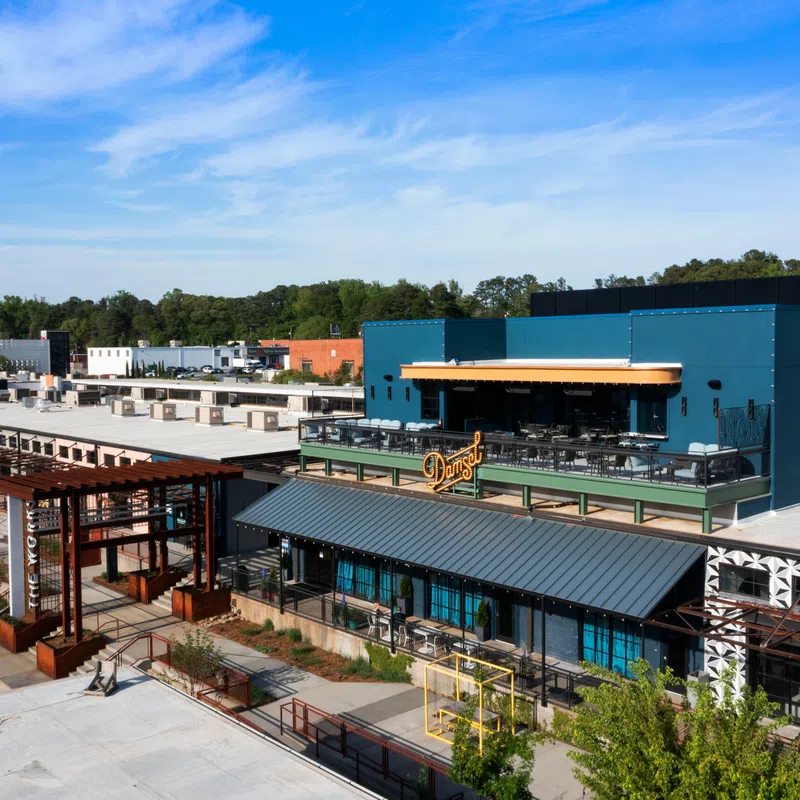 Modern commercial complex with industrial design, outdoor seating, and blue sky on a sunny day.