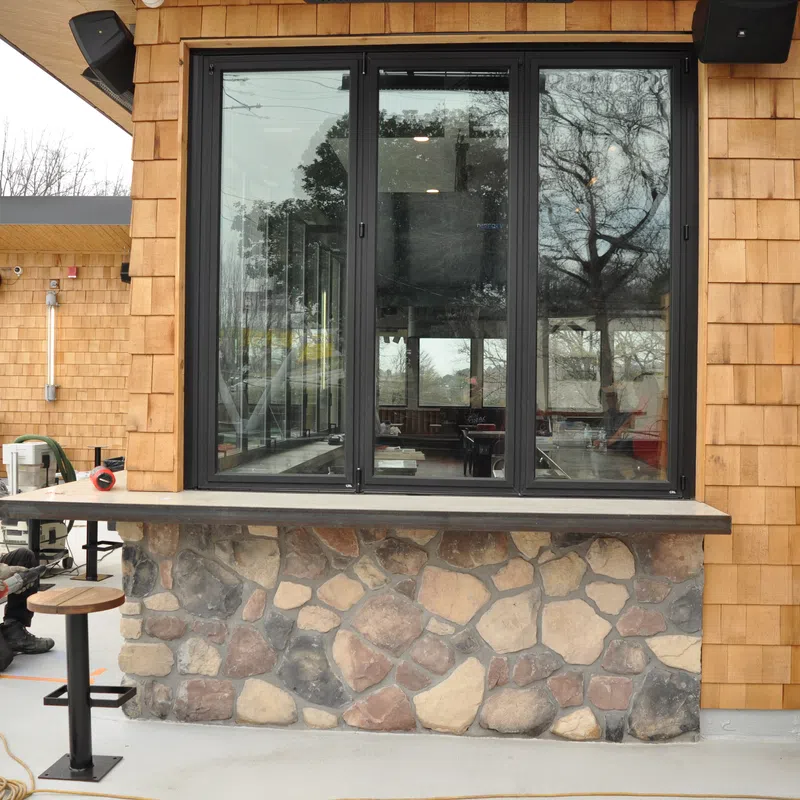 Man working on outdoor seating area with stone and wood siding during construction or renovation.