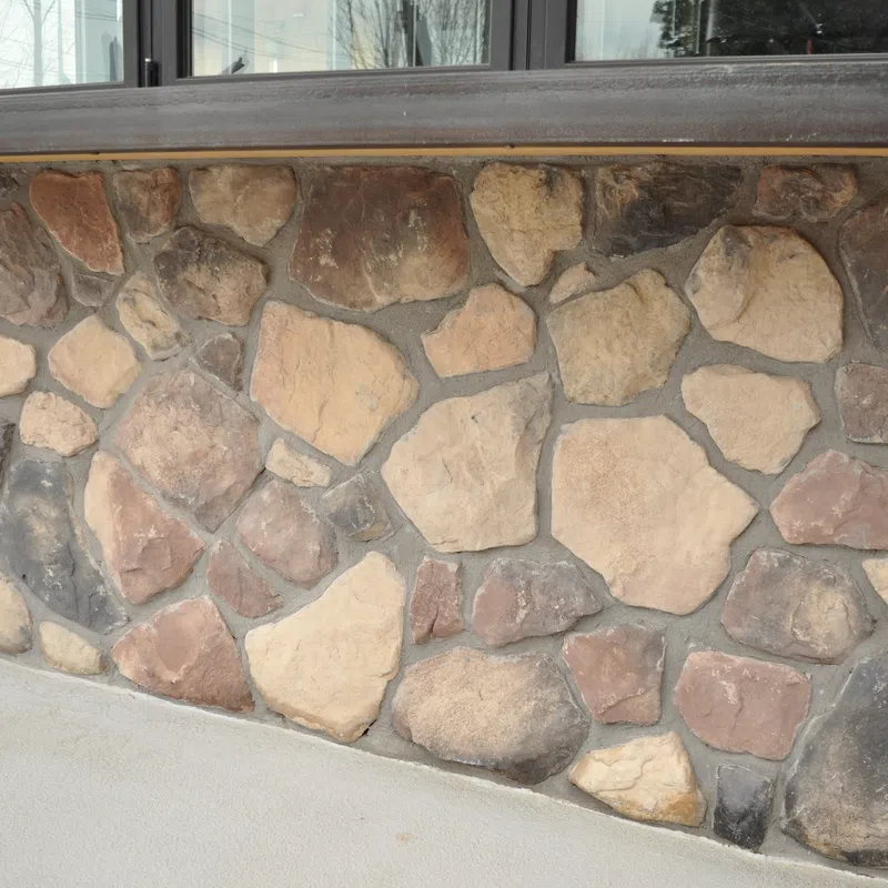 Rustic stone wall facade with various shades of brown and gray stones under a wooden ledge.