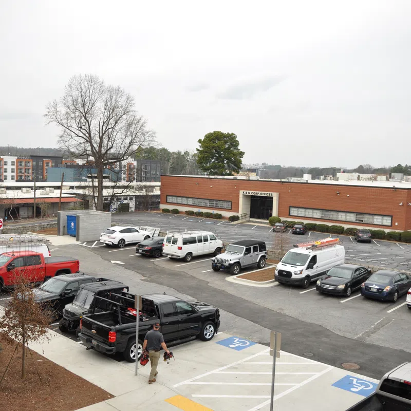 Urban parking lot with various vehicles, including trucks and vans, in front of a brick commercial building on a cloudy day.